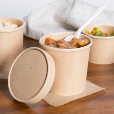 three cups with food in them sitting on a wooden table next to a napkin and bag