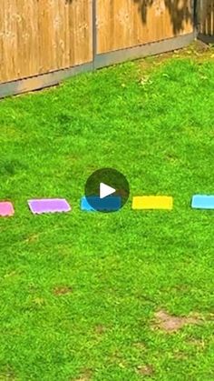 a child is playing with colored blocks in the grass near a wooden fence and tree