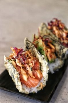 two sushi rolls with toppings on a black plate