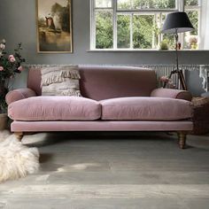 a pink couch sitting in front of a window next to a vase with flowers on it