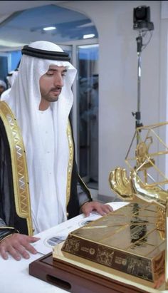 a man in a white and gold outfit looking at a piece of paper on a table