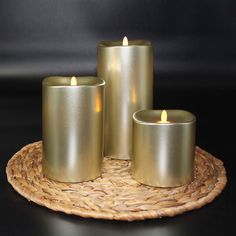 three gold colored candles sitting on top of a wicker place mat next to each other