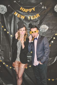 two people standing in front of a happy new year backdrop with glasses on their mouths