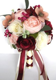 a bridal bouquet with pink and red flowers on it's side, tied in burgundy ribbon