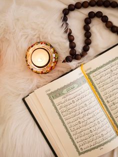 an open book with arabic writing next to a candle