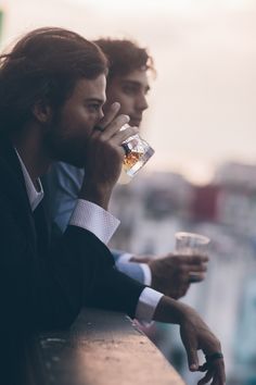 two men sitting next to each other drinking