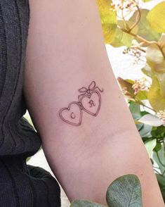 a woman's arm with two hearts and a bow tattoo on the left forearm