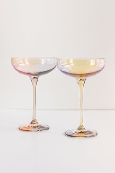 two wine glasses sitting next to each other on a white counter top in front of a wall