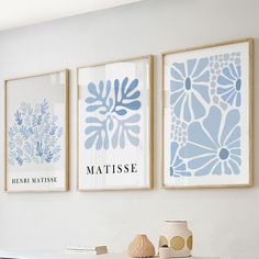 three blue and white art prints hanging on the wall above a table with vases