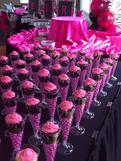 there are many cupcakes on the table with pink frosting and candy cones