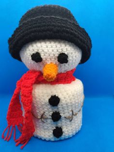 a crocheted snowman wearing a black hat and red scarf on a blue background