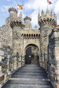 the entrance to an old castle with flags flying in the air and stone walls on either side