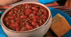 a blue plate topped with a bowl of chili next to a piece of bread on top of a table