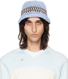 a man with long hair wearing a blue knitted hat and white sweater is looking at the camera