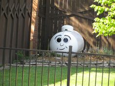 a large white tank sitting in the middle of a yard next to a fence and trees