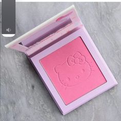 a hello kitty face powder in a pink box on a gray surface with the lid open