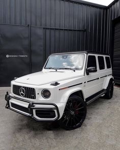 a white mercedes benz g63 is parked in front of a building with black shutters