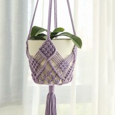 a purple macrament hanging from a window sill with a plant in it