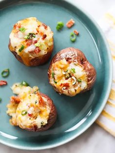 three baked potatoes on a blue plate topped with cheese and green onion garnish