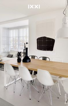 a dining room table with white chairs and black vases on top of the table