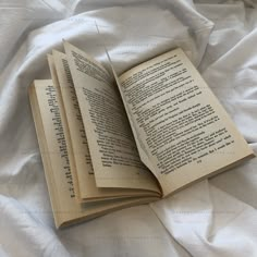 an open book sitting on top of a bed next to a white sheet and pillows