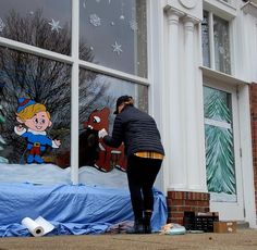 a woman is painting a window on the side of a building with snowflakes