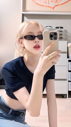 a woman in sunglasses taking a selfie with her cell phone while sitting on the floor