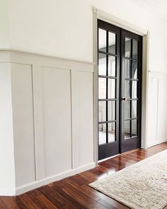 an empty room with wooden floors and black doors on either side of the door is a large rug