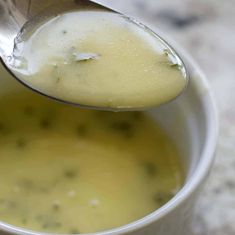 a spoon full of soup is being held over the top of a white cup filled with broth