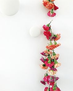 flowers are hanging from the ceiling next to two white balls and a vase with red, orange and pink flowers on it