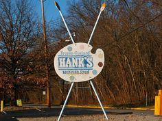 a sign for hank's with two golf clubs sticking out of it and trees in the background