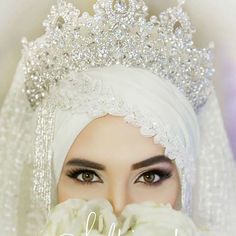 a woman wearing a tiara and veil with flowers in her hands, covering her mouth