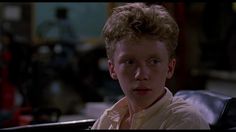 a young man with blonde hair sitting in a chair looking at the camera while wearing a white shirt