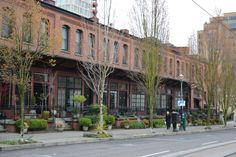 two people are walking down the street in front of some old brick buildings and trees