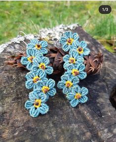 two crocheted flowers are sitting on a piece of wood next to pine cones