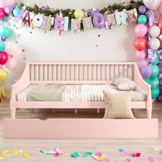 a pink bed with balloons and streamers on the wall