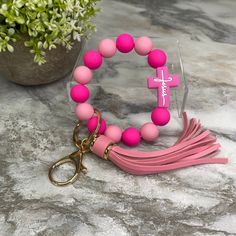 a pink bracelet with a cross and tassel is on a marble table next to a potted plant