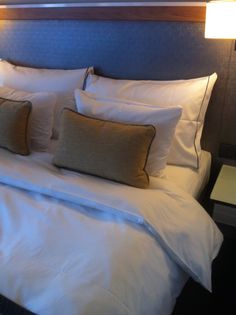 a neatly made bed with white sheets and brown pillows on top of the headboard