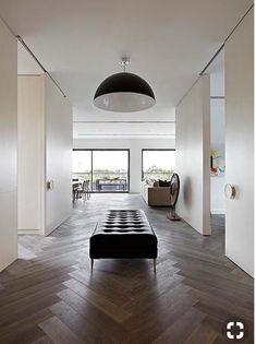 a living room with wood flooring and white walls, along with a black ottoman