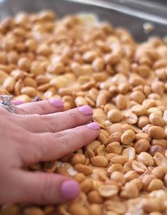 a woman's hand reaching for some food in a pan with peanuts on it