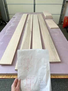 a person holding up a piece of paper next to wooden planks on top of a table