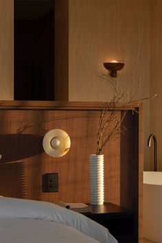 a white vase sitting on top of a bed next to a night stand and lamp