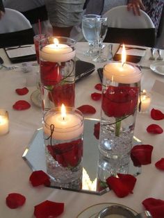 several candles are placed in glass vases with roses on the table