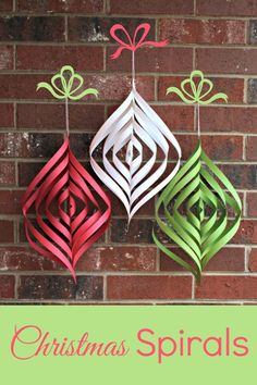 three paper ornaments hanging on a brick wall with the words christmas spirals below them