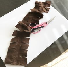 a pair of pink scissors sitting on top of a piece of paper cut into strips