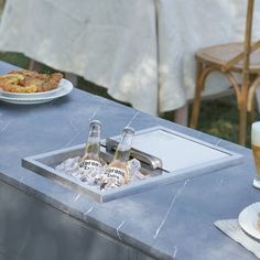 two beer bottles are sitting on an outdoor table with food and drinks in front of them