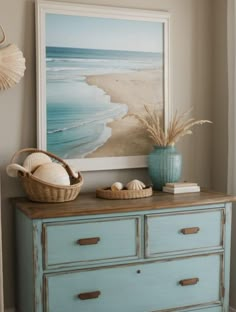 a blue dresser with two baskets on top of it and seashells in the bottom drawer