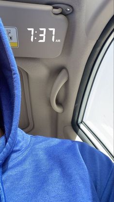 a person wearing a blue hoodie sitting in the back seat of a car with an alarm clock on it