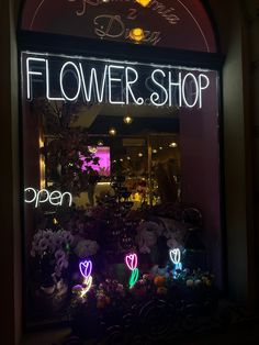 a flower shop with flowers in the window and neon lights on it's windows