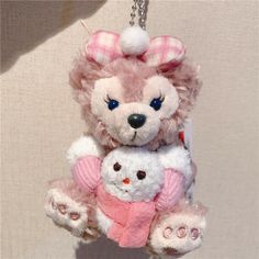 a pink teddy bear holding a white stuffed animal in it's arms, hanging from a chain